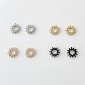 May include: Six pairs of earrings with a sunburst design. The earrings are available in silver, gold, and black.