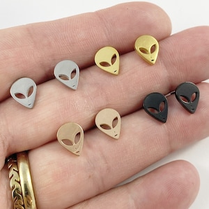 May include: A set of six alien head stud earrings in various metal finishes: silver, gold, rose gold, and black.