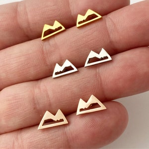 May include: Five pairs of mountain-shaped earrings in gold, silver, and rose gold. The earrings are small and delicate, and they would make a great gift for a nature lover.