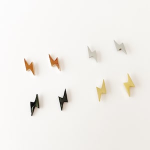 May include: Eight small lightning bolt shaped metal charms in different colours, including gold, silver, and black.