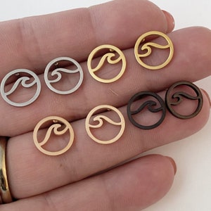 May include: A set of six wave earrings in different metal finishes, including gold, silver, and bronze. The earrings are all circular with a wave design cut out of the center.