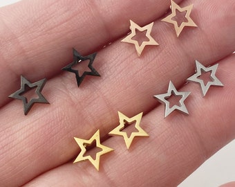 May include: Six pairs of star-shaped earrings in different colors. The earrings are made of metal and have a hollow center. The colors are gold, silver, and black.
