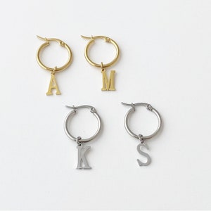 Peut inclure: Quatre paires de boucles d'oreilles créoles avec des breloques en forme de lettres. Deux paires sont dorées avec les lettres A et M. Deux paires sont argentées avec les lettres K et S.