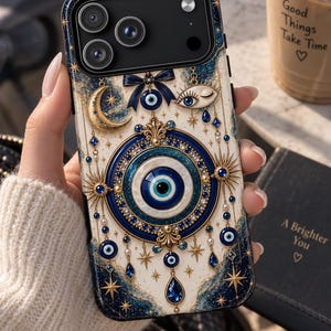 May include: A smartphone case featuring a central blue and white evil eye motif surrounded by gold celestial elements, including a crescent moon, stars, and a winking eye. The design includes dark blue accents, hanging charms, and glittery details.