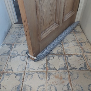 May include: A blue and white patterned doorstop with a chevron design. The doorstop is placed under a wooden door.