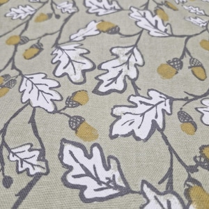 May include: A close-up of a light green fabric with a white and grey oak leaf pattern. The leaves are outlined in grey and have a white centre. There are small yellow acorns scattered throughout the pattern.