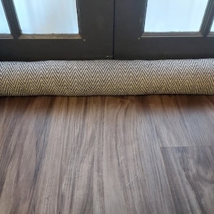 May include: A brown and white patterned doorstop made of fabric. The doorstop is lying on a wooden floor.