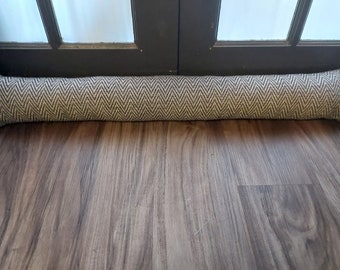 May include: A brown and white patterned doorstop made of fabric. The doorstop is lying on a wooden floor.