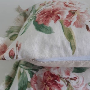 May include: Two white pillow covers with a floral pattern featuring pink and green flowers. The pillow covers have a zipper closure with a rose gold zipper pull.