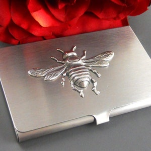 K&ouml;nnte beinhalten: Ein silberner Visitenkartenhalter aus Metall mit einem 3D-Bienendesign. Die Biene ist silberfarben und hat detaillierte Fl&uuml;gel und Beine.
