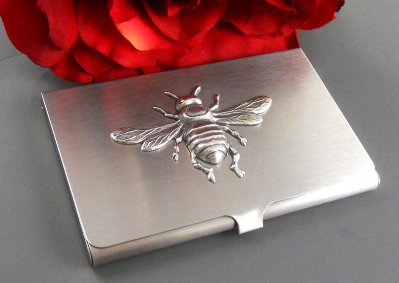 K&ouml;nnte beinhalten: Ein silberner Visitenkartenhalter aus Metall mit einem 3D-Bienendesign. Die Biene ist silberfarben und hat detaillierte Fl&uuml;gel und Beine.
