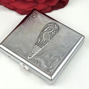 May include: A silver cigarette case with an engraved design of a bird and floral pattern.
