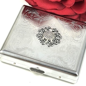 May include: Silver cigarette case with an ornate design and a decorative turtle charm.