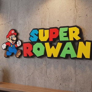 May include: A wall-mounted sign featuring a cartoon character in a red hat, blue overalls, and brown shoes, positioned next to the text SUPER ROWAN in a bold, multi-coloured block font with black outlines, displayed against a grey concrete wall.