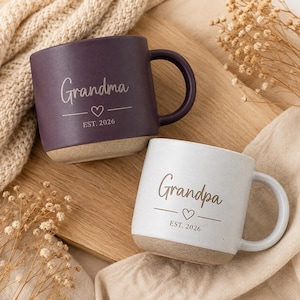 Peut inclure: Deux tasses en céramique avec une finition mate, une violet foncé et une blanche avec des taches. Les deux présentent une base de couleur claire, une anse et le texte imprimé "Grandma" ou "Grandpa" au-dessus d'un petit cœur et "EST. 2026".