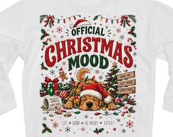 Op de afbeelding: Een wit sweatshirt met lange mouwen en een afbeelding van een golden retriever met een kerstmuts, omringd door kerstverlichting, cadeaus, een boom en een mok. De tekst luidt OFFICIAL CHRISTMAS MOOD, SAME ME JUST MORE CHRISTMAS en EAT DRINK BE MERRY REPEAT.