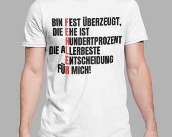 Op de afbeelding: Een wit t-shirt met korte mouwen en zwarte Duitse tekst: BIN FEST ÜBERZEUGT, DIE EHE IST HUNDERTPROZENT DIE ALLERBESTE ENTSCHEIDUNG FÜR MICH! Het woord FEHLER is verticaal in rode letters gemarkeerd binnen de tekst op het shirt.