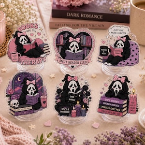 May include: Six acrylic standees featuring a black-cloaked figure with a white mask and pink bow reading books. Designs include text like BOOKS are my THERAPY, SMUT READER CLUB, JUST ONE MORE CHAPTER, and stacks of books with titles like SPICY STORIES.