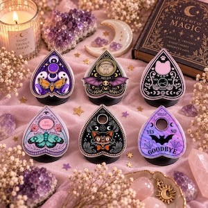 May include: Six heart-shaped planchette phone grips featuring various designs including a moth, a bat, a cat face, a butterfly, a cat head, and a bat silhouette. Each piece displays text such as 'Good Bye', 'Hello', 'Meow', 'Yes', and 'No' in a decorative style.