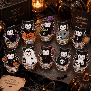 May include: A collection of ten acrylic vampire character figures, each mounted on a clear circular base. The characters feature various Halloween themes including pumpkins, cauldrons, tombstones with RIP text, brooms, ghosts, and skulls.