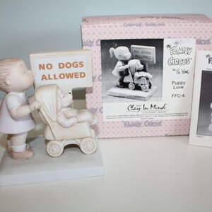 May include: A ceramic figurine set from "The Family Circus" collection. It features a girl kissing a dog in a stroller, with a sign that reads "NO DOGS ALLOWED." The set includes a box and a card with illustrations.