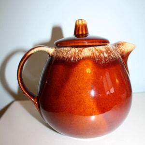 May include: A brown ceramic teapot with a lid and handle. The teapot has a glossy finish and a rounded shape. The rim of the teapot has a lighter, speckled design. The teapot is designed for brewing tea.