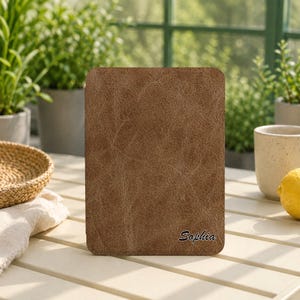 May include: A rectangular brown tablet or e-reader case with a textured, distressed leather-like finish. The bottom right corner features the name Sophia printed in a black, cursive script font. The case has rounded corners and a flat surface.