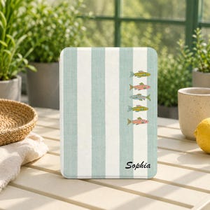 May include: A rectangular e-reader cover featuring a vertical striped pattern in light sage green and white. The cover displays a column of five small, colorful fish illustrations and the name Sophia printed in black script at the bottom right.
