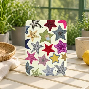 May include: A rectangular tablet case with a cream background featuring a pattern of multi-coloured stars in various textures and designs, including zebra print, sequins, and embroidery. The name Sophia is printed in black script in the bottom right.