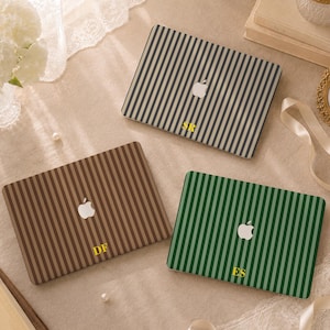 May include: Three rectangular laptop covers featuring vertical stripes in black, brown, and green. Each cover displays a centred white Apple logo and personalised yellow initials at the bottom, specifically SR on the black, DF on the brown, and ES on the green.