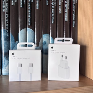 Może przedstawiać: Dwa białe pudełka produktów Apple. Lewe pudełko przedstawia kabel ładujący USB-C 60W (1m) z ilustracją przewodu. Prawe pudełko przedstawia zasilacz USB-C 20W z ilustracją białej wtyczki z dwoma metalowymi bolcami.