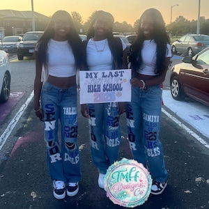 May include: Three individuals wearing white short-sleeved crop tops and blue denim jeans customized with white and blue lettering that reads "SENIOR," "CLASS OF 25," and "LHS EAGLES." They hold a sign that says "MY LAST FIRST DAY OF HIGH SCHOOL 2025."