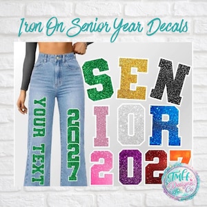 May include: Light blue denim jeans featuring green glitter iron-on decals that read YOUR TEXT and 2027. The image displays various glittery letter and number decals in green, gold, black, pink, silver, blue, purple, red, and orange colors.