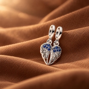 Puede incluir: Un charm de plata de ley con dos alas de ángel simétricas que forman un corazón. Las alas están adornadas con pequeñas piedras redondas azules y transparentes. El lateral del charm tiene grabado el texto S925 ALE.