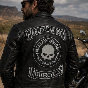 May include: A black leather jacket featuring a large back patch with the text Harley-Davidson Motorcycles and a central skull graphic. The jacket has a classic collar, metal snap buttons at the hem, and prominent white embroidered lettering.