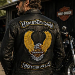 May include: A black leather jacket featuring a large embroidered patch on the back. The patch displays a yellow eagle with spread wings, the text Harley-Davidson Motorcycles, and the Harley-Davidson logo in white, yellow, and black embroidery.