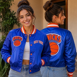 May include: A royal blue satin bomber jacket featuring orange and white striped ribbed trim at the collar, cuffs, and hem. The front displays an embroidered New York Knicks logo and text, while the back features a large Knicks logo graphic.