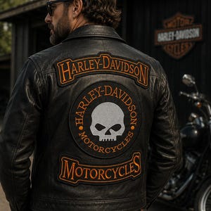 Op de afbeelding: Een zwart leren jack met grote geborduurde patches op de rug. De bovenste patch bevat de tekst Harley-Davidson in oranje. De centrale ronde patch toont een grijze schedel met de tekst Harley-Davidson Motorcycles.