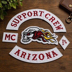 May include: A set of embroidered patches featuring a white arched top rocker with red text reading SUPPORT CREW, a white bottom rocker with red text reading ARIZONA, a rectangular MC patch, a diamond 1% patch, and a skull graphic with flames.