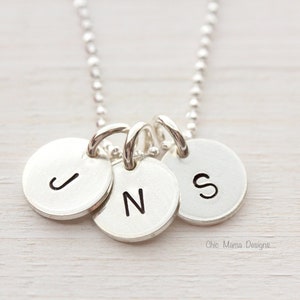 May include: Silver necklace with three round charms, each with a letter engraved on it. The letters are J, N, and S.