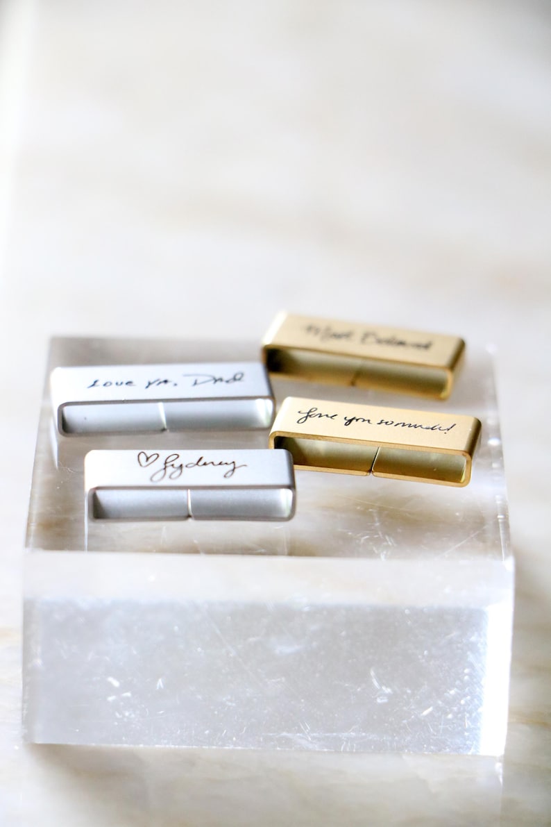 Może przedstawiać: Cztery prostokątne, spersonalizowane pendrive'y z odręcznymi wiadomościami. Dwa są srebrne, a dwa złote. Wiadomości to "love ya, Dad", "Sydney", "love you so much!" i "To Joel, Beloved". Pendrive'y są wyświetlane na przezroczystym, prostokątnym bloku.