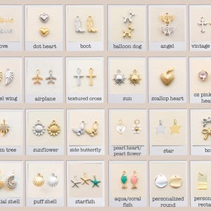 Op de afbeelding: Een verzameling kleine metalen bedels gerangschikt in een raster, met diverse vormen zoals harten, kruisen, dieren, hemelse symbolen, schelpen en strikken in goud- en zilvertinten, elk gelabeld met de specifieke naam van het ontwerp.