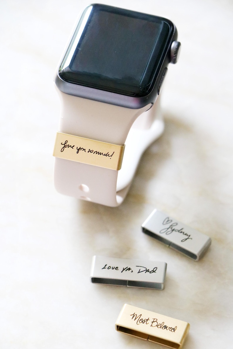 Może przedstawiać: Apple Watch z jasnor&oacute;żowym paskiem i złotą opaską z napisem "Love you so much!". Widoczne są trzy dodatkowe opaski, każda z innym napisem.