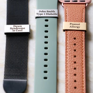 Może przedstawiać: Trzy paski do Apple Watch w układzie pionowym. Pierwszy to czarna siatka z napisem "Down Syndrome is Cool". Drugi to jasnozielony silikonowy pasek z napisem "John Smith Type 1 Diabetic". Trzeci to brązowy sk&oacute;rzany pasek z napisem "Peanut Allergy".
