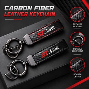 Könnte beinhalten: Zwei Schlüsselanhänger aus schwarzem Carbon und Leder mit dem rot-weißen Schriftzug ST Line. Jeder Schlüsselanhänger verfügt über einen dunklen Metallring und einen kleineren Ring. Das Design zeigt eine gewebte Carbonstruktur und rote Nähte.