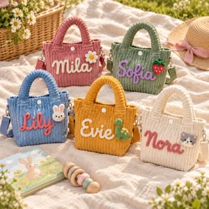 Puede incluir: Cinco bolsos pequeños de pana en rosa, verde, azul, amarillo y crema. Cada bolso tiene un cierre de presión blanco, una correa desmontable y un nombre personalizado en letras en relieve, junto a un pequeño animal o fruta de ganchillo.