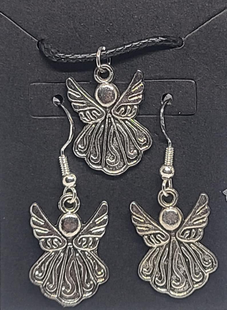 May include: A silver angel pendant necklace and matching earrings. The angel has detailed wings and a halo. The necklace is on a black cord.