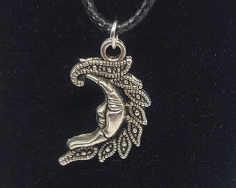May include: A silver crescent moon pendant necklace with a detailed design. The pendant is attached to a black cord.