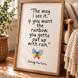 May include: A rectangular framed wall art piece featuring a light wood frame and a white background. The text reads, "The way I see it, if you want the rainbow, you gotta put up with rain." Below the text is a watercolour rainbow butterfly and the name Dolly Parton.