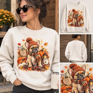 Puede incluir: Una sudadera de cuello redondo color crema con un gráfico de un bulldog francés que lleva un gorro de punto naranja y una bufanda de cuadros. El perro está rodeado de calabazas, hojas de otoño, un farol y un cartel que dice Hello fall.